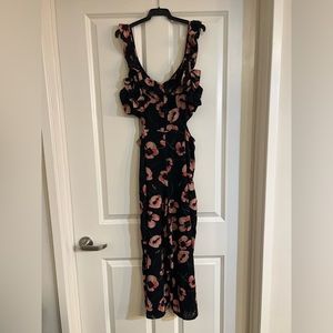 Black wide leg jumpsuit with floral pattern. Side cut out with ruffled staps